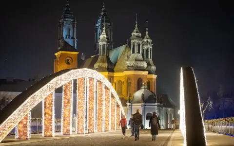Most Jordana nocą, ozdobiony tysiącami światełek, z katedrą w tle. Spacerujący ludzie podziwiają iluminacje.