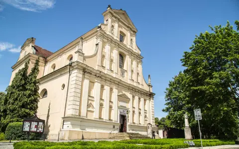 Jasny kościół Karmelitów w Poznaniu z zielenią i błękitnym niebem.