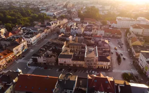 Widok z lotu ptaka na szamotuły rynek z kolorowymi kamienicami i ulicami oświetlonymi zachodzącym słońcem.