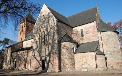Kamienna budowla z ceglaną wieżą, z cieniem drzew na ścianach, w stylu romańskim, przed gotykiem.