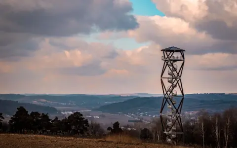 Wieża widokowa na tle malowniczego krajobrazu z pagórkami i chmurami.