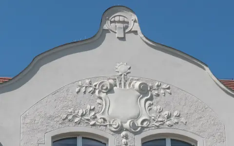 Ozdobny detal architektoniczny w stylu secesja w Poznaniu: tarcza z motywami roślinnymi i groteskowa twarz na szczycie.