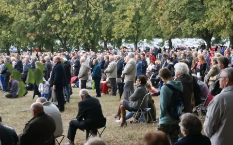 Tłum ludzi zgromadzony na trawie, drzewa w tle. Odpust w Bieniszewie przyciągnął wielu wiernych.