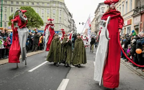 Parada z okazji św. Marcina. Postacie na szczudłach w czerwonych strojach i dzieci w zielonych płaszczach idą ulicą. Legenda o św. Marcinie ożywa.