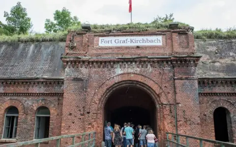 Wejście do Fortu Graf-Kirchbach, historycznej twierdzy w Poznaniu. Grupa turystów wchodzi do ciemnego tunelu.