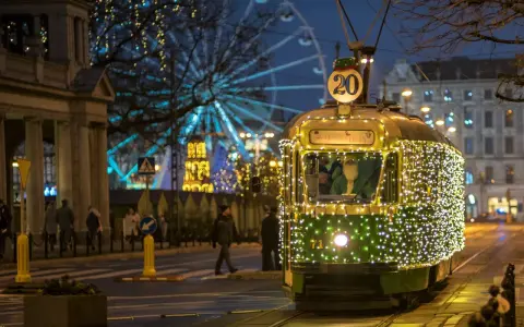 Świąteczny tramwaj po poznańsku, ozdobiony tysiącami lampek, mknie przez miasto. W tle widać diabelski młyn i iluminacje.