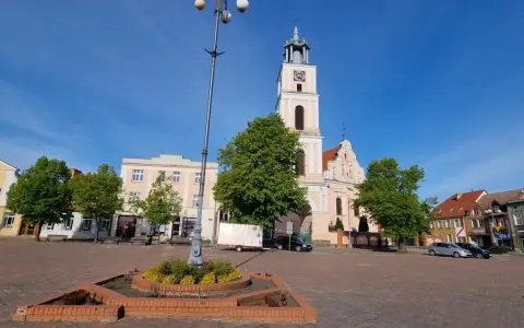 Rynek w Chodzieży Wielkopolskiej z kościołem i kamienicami. Słoneczny dzień, błękitne niebo.