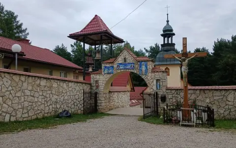 Kamienny łuk z mozaikami i dzwonnicą prowadzi do klasztoru, jednego z wielu pustelni w Polsce. Obok krzyż z Jezusem.