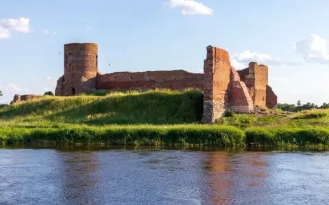 Ruiny zamku w Kole, z charakterystyczną okrągłą wieżą, stoją dumnie na zielonym wzgórzu nad rzeką.