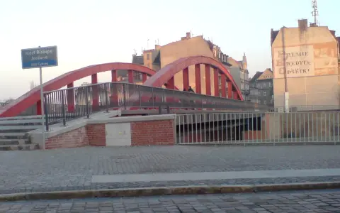 Czerwony most Biskupa Jordana z kłódkami na balustradach, otoczony kamienicami.