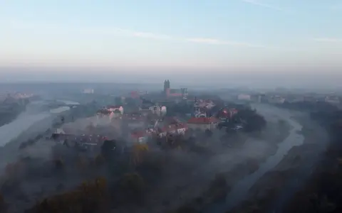Mglisty poranek nad rzeką, wyłaniający się z mgły **Ostrów Tumski Poznań** z katedrą i zabytkową zabudową.