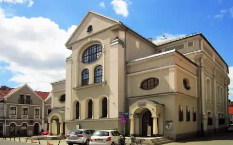 Jasny budynek z charakterystycznymi oknami, jeden z leszczyńskich zabytków, stoi na tle błękitnego nieba z chmurami.