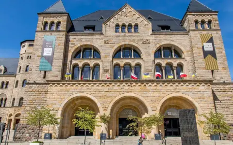 Kamienny pałac cesarski z łukowymi oknami i wieżyczkami. Na fasadzie flagi i banery informujące o Centrum Kultury Zamek i kinie pałacowym.