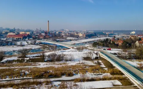 Zimowy krajobraz z nowoczesnymi mostami berdychowskimi, rzeką i panoramą miasta w tle.