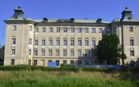 Imponujący pałac, największy zamek w Wielkopolsce, z zielonymi dachami i licznymi oknami, otoczony drzewami i trawą.