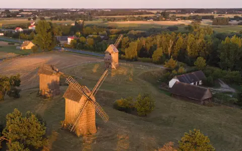 Trzy drewniane wiatraki na tle krajobrazu, przypominające o dawnych pojezierza w polsce.