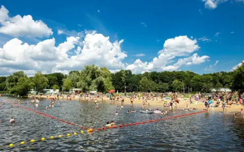 Tłum ludzi odpoczywa na plaży i kąpie się w jeziorze w Poznaniu. Słoneczny dzień, błękitne niebo z chmurami.