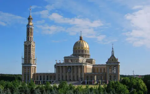 Imponujące sanktuarium koło Konina z wysoką wieżą i złotą kopułą, otoczone zielenią.