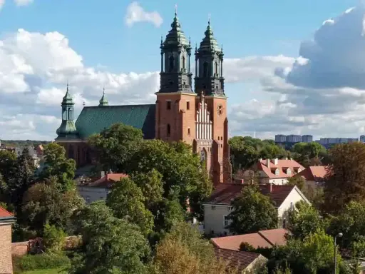 Majestatyczna poznańska katedra z zielonym dachem i dwiema wieżami góruje nad drzewami i budynkami.