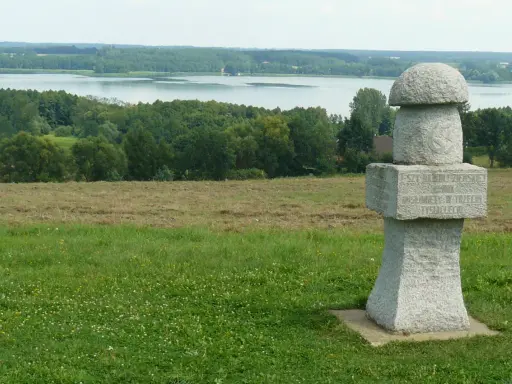 Kamienny, wielki grzyb z inskrypcją stoi na wzgórzu. W tle jezioro i las.