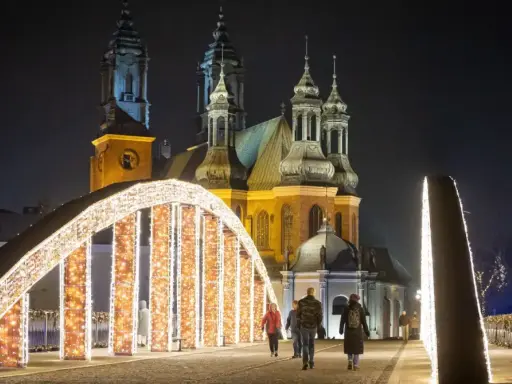 Most Jordana nocą, ozdobiony tysiącami światełek, z katedrą w tle. Spacerujący ludzie podziwiają iluminacje.