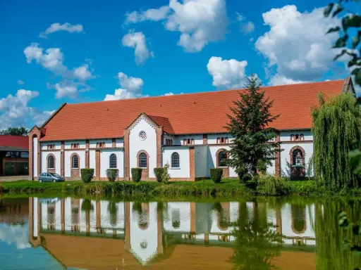Pałac w Racocie z czerwonym dachem i białymi ścianami odbija się w spokojnej tafli wody.
