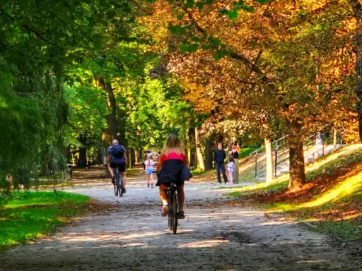 Kalisz wydarzenia weekend: ludzie jeżdżą na rowerach i spacerują alejkami parku w jesiennym słońcu.