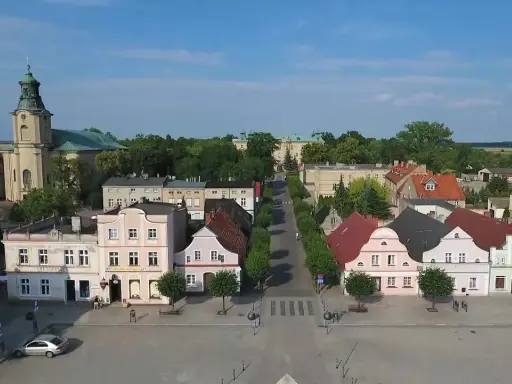 Rydzyna atrakcje: malowniczy rynek z kolorowymi kamieniczkami, kościołem i pałacem w tle.