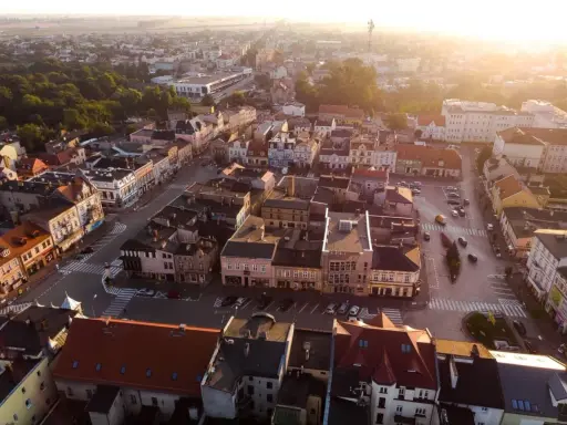 Widok z lotu ptaka na szamotuły rynek z kolorowymi kamienicami i ulicami oświetlonymi zachodzącym słońcem.