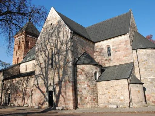 Kamienna budowla z ceglaną wieżą, z cieniem drzew na ścianach, w stylu romańskim, przed gotykiem.