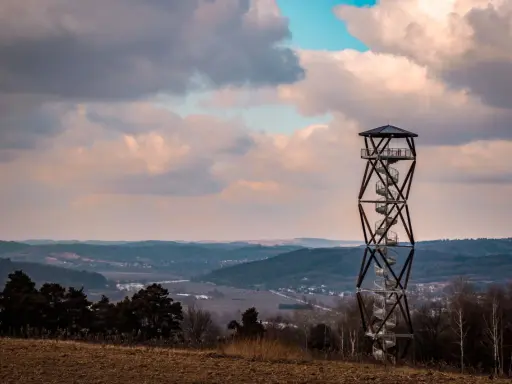 Wieża widokowa na tle malowniczego krajobrazu z pagórkami i chmurami.