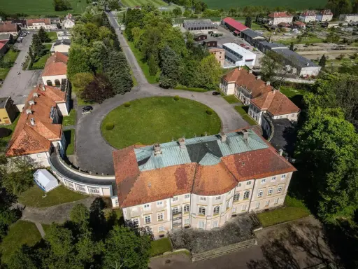Pałac w Pawłowicach z lotu ptaka, otoczony zielenią i innymi budynkami.