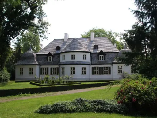 Malowniczy dwór w Koszutach otoczony zielenią. Klasyczna architektura z wieżyczkami i mansardowym dachem.