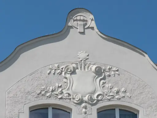 Ozdobny detal architektoniczny w stylu secesja w Poznaniu: tarcza z motywami roślinnymi i groteskowa twarz na szczycie.