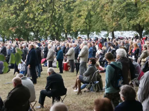 Tłum ludzi zgromadzony na trawie, drzewa w tle. Odpust w Bieniszewie przyciągnął wielu wiernych.