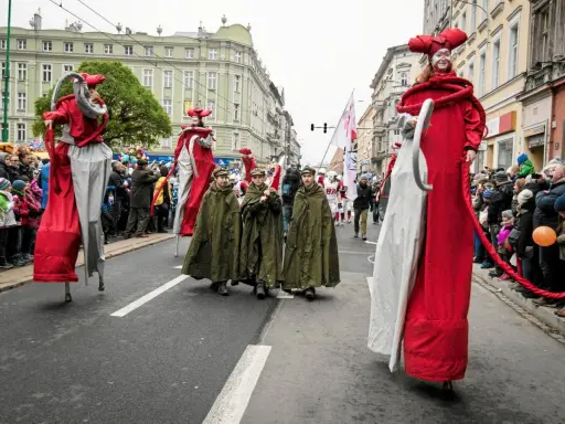 Parada z okazji św. Marcina. Postacie na szczudłach w czerwonych strojach i dzieci w zielonych płaszczach idą ulicą. Legenda o św. Marcinie ożywa.