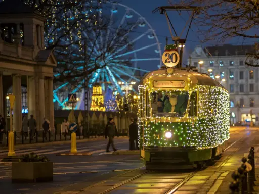 Świąteczny tramwaj po poznańsku, ozdobiony tysiącami lampek, mknie przez miasto. W tle widać diabelski młyn i iluminacje.