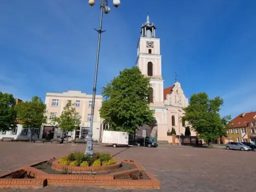 Rynek w Chodzieży Wielkopolskiej z kościołem i kamienicami. Słoneczny dzień, błękitne niebo.
