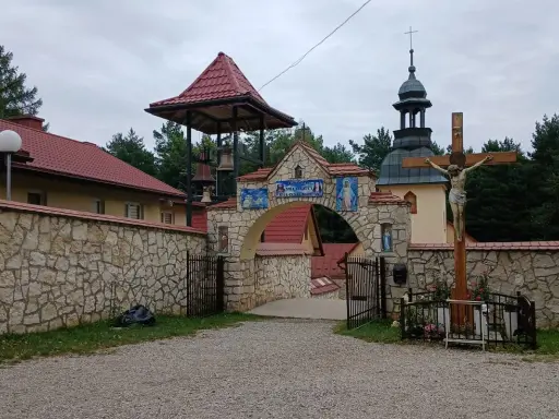Kamienny łuk z mozaikami i dzwonnicą prowadzi do klasztoru, jednego z wielu pustelni w Polsce. Obok krzyż z Jezusem.
