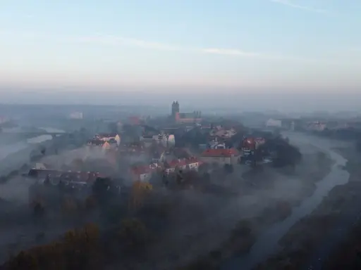 Mglisty poranek nad rzeką, wyłaniający się z mgły **Ostrów Tumski Poznań** z katedrą i zabytkową zabudową.