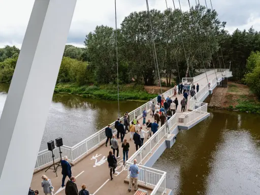 Uroczyste otwarcie kładki owińskiej. Ludzie spacerują po nowoczesnym moście wiszącym nad rzeką, otoczonym zielenią.
