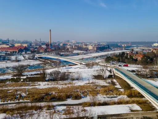 Zimowy krajobraz z nowoczesnymi mostami berdychowskimi, rzeką i panoramą miasta w tle.