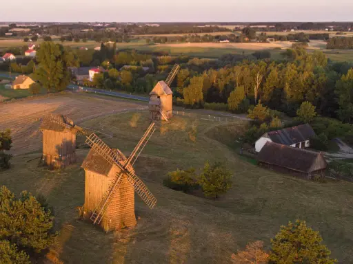 Trzy drewniane wiatraki na tle krajobrazu, przypominające o dawnych pojezierza w polsce.