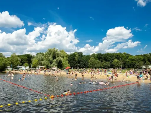 Tłum ludzi odpoczywa na plaży i kąpie się w jeziorze w Poznaniu. Słoneczny dzień, błękitne niebo z chmurami.