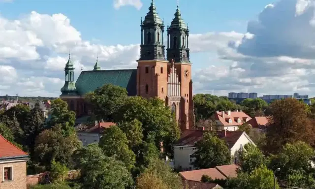 Majestatyczna poznańska katedra z zielonym dachem i dwiema wieżami góruje nad drzewami i budynkami.