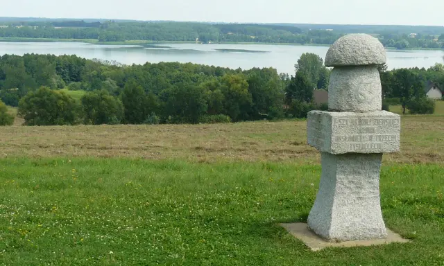 Kamienny, wielki grzyb z inskrypcją stoi na wzgórzu. W tle jezioro i las.