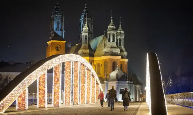 Most Jordana nocą, ozdobiony tysiącami światełek, z katedrą w tle. Spacerujący ludzie podziwiają iluminacje.