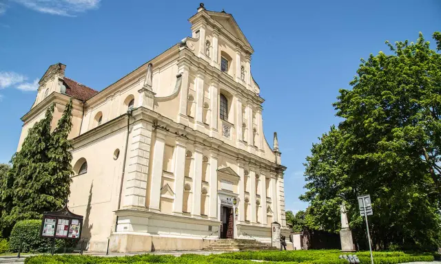 Jasny kościół Karmelitów w Poznaniu z zielenią i błękitnym niebem.