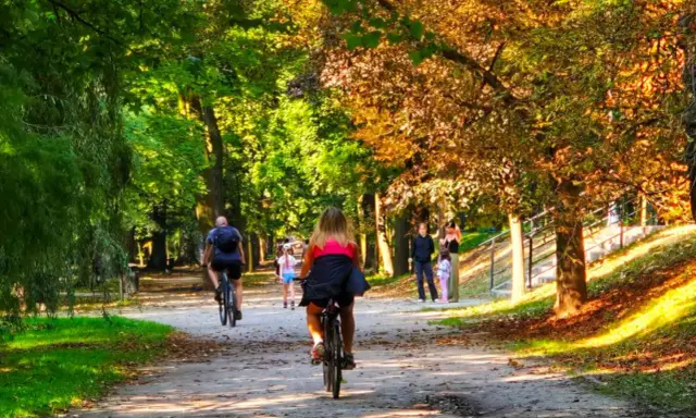 Kalisz wydarzenia weekend: ludzie jeżdżą na rowerach i spacerują alejkami parku w jesiennym słońcu.