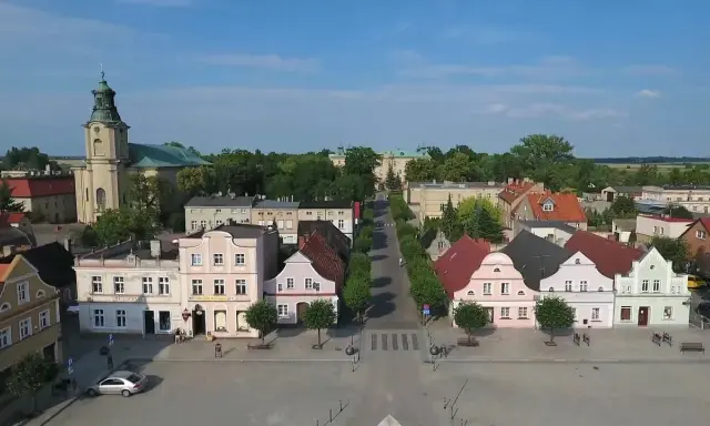 Rydzyna atrakcje: malowniczy rynek z kolorowymi kamieniczkami, kościołem i pałacem w tle.